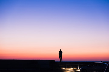 silhouette of a lonely standing man standing against the sunset sky blue with red