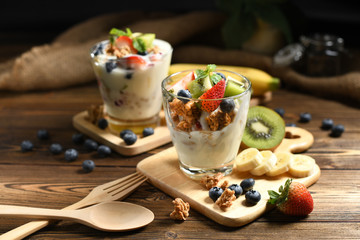 Yogurt with granola and fruits in glass on wooden table