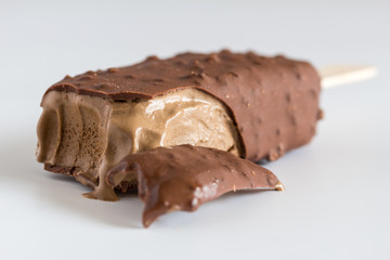 Chocolate ice cream on stick with selective focus on bitten front part isolated on white grey background