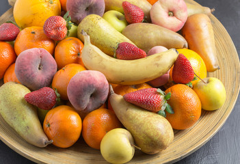 Fruit bowl with exotic whole fruits close up in rustic wooden bowl