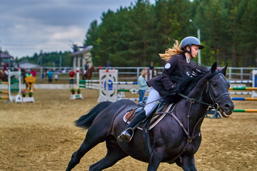 Young woman jockey in white black dress and black boots, takes part in equestrian competitions....