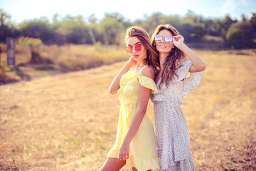 two pretty womem walking in the field dressed in summer dresses and sunglasses and having fun