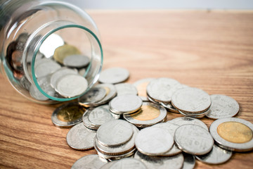 Close up of money coins Thai baht in and outside the glass jar on the wood table.