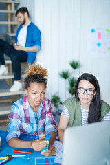 Portrait of two creative young women using computer for internet networking while working at desk in office