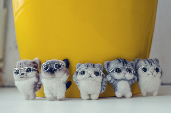 Felting toy little kittens with glasses around yellow pot