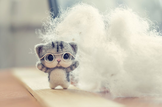 Felting toy small gray kitten in glasses on wooden stand, wool on background