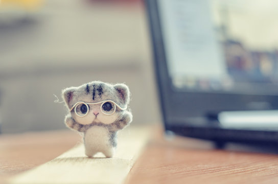Felting toy little gray kitten in glasses on wooden stand