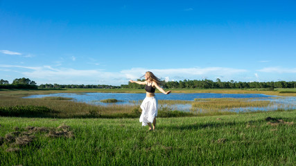 Beautiful young spiritual blonde woman long hair dancing and spinning in a field next to a lake white skirt
