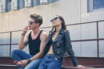 young stylish man smoking cigarette near his beautiful girlfriend in sunglasses