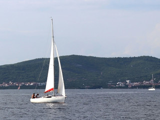 A small sailing sports yacht of daytime sailing is sailing with three yachtsmen along the coast of Croatia. Water sports and summer vacation on the water on a sunny summer day. A fascinating lifestyle