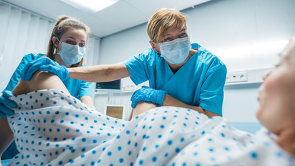 In the Hospital Professional Midwives Helping Spread Legs to Woman Pushes to Give Birth in Labor....