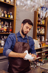 Cleaning glasses. Confident experienced barman looking attentively at the glass in his hand while cleaning it