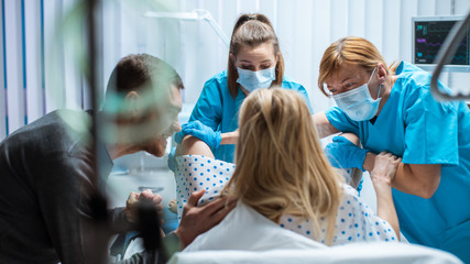 In the Hospital Woman Giving Birth, Husband Holds Her Hand in Support, Obstetricians Assisting....