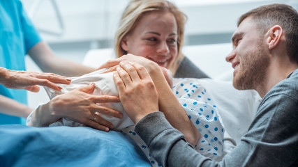 Fototapeta In the Hospital Midwife Gives Newborn Baby to a Mother to Hold, Supportive Father Lovingly Hugging Baby and Wife. Happy Family in the Modern Delivery Ward. obraz