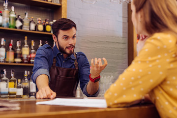 Detailed explanation. Calm professional barman standing at the bar counter and looking at the...