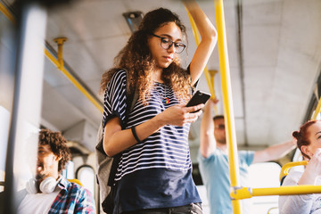 Curly young student girl holding for a bar in a public transportation and listening to the music...