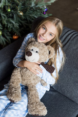 high angle view of adorable happy child hugging teddy bear and smiling at camera at christmas time