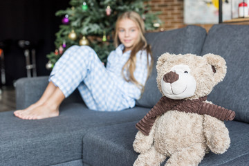 close-up view of teddy bear and child in pajamas sitting on couch behind at christmas time