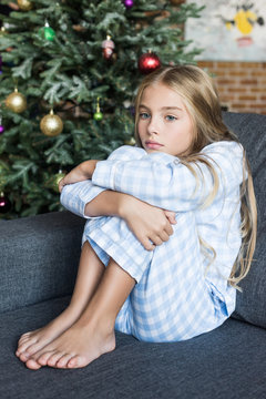 Upset Child In Pajamas Sitting On Sofa At Christmas Time