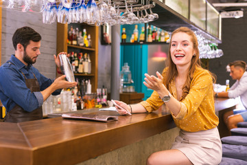 Sudden meeting. Cheerful young girl sitting at the bar counter and smiling while noticing her friends