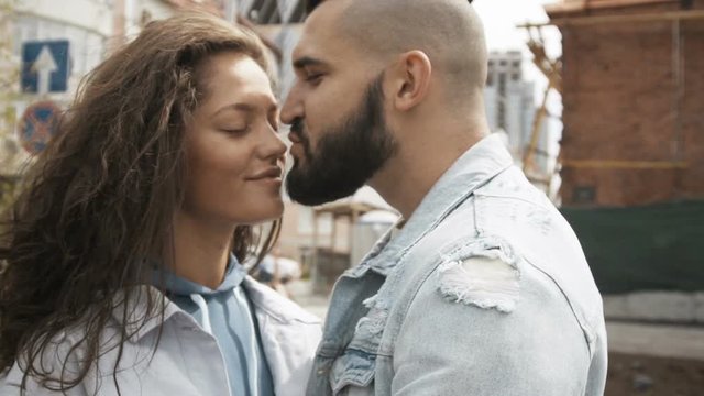 Beautiful young woman and bearded man kissing with love standing on street