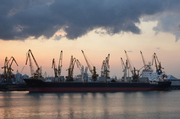 Fototapeta premium Cargo ship and cranes in the port, reflected in the water, twilight.