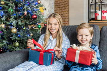 Fototapeta na wymiar cute happy kids in pajamas holding presents and smiling at camera at christmas time