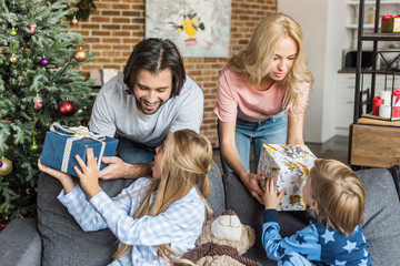 parents presenting christmas gifts to happy children in pajamas