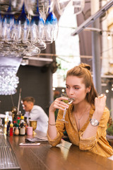 Thoughtful client. Calm young girl sitting in the bar and thoughtfully drinking her alcohol