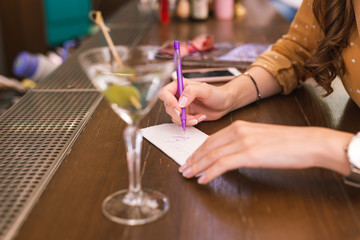 Writing number. Young girl sitting at the bar counter and writing her phone number on the piece of paper