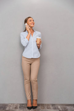Happy business woman standing over grey wall background talking by mobile phone.