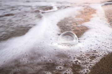Large Glass Ball Swamped by White Ocean Foam on Beach