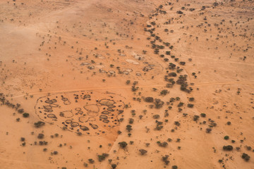 A top-down, aerial view of a traditional circular village of huts and animal enclosures next to a dry river bed in the arid Kaisut desert near Marsabit, northern Kenya