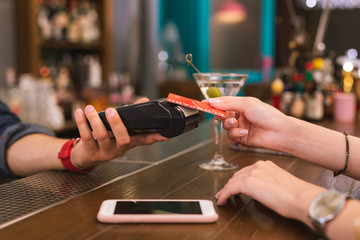 Quick payment. Progressive young girl using her club card while paying the bill in the bar