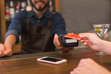 Paying easily. Positive friendly barman smiling while the client paying by card