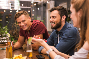 Friendly meeting. Positive young friends having good time and smiling while sitting in the bar