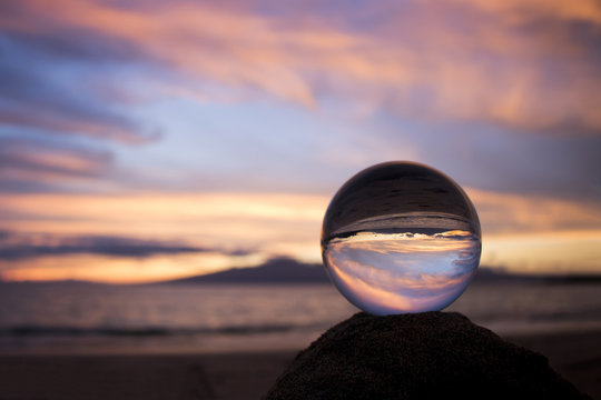 Pink Clouds at Sunset over Ocean with Island Captured in Glass Ball