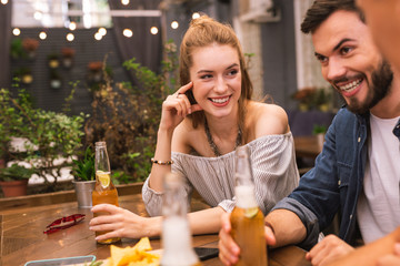 Cute company. Cheerful young girl smiling to her friends while looking at them in the bar