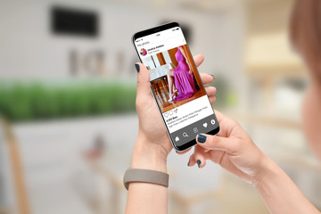 Girl looking at publicly shared photo on social network on her phone. Girl promoting elegant purple dress on social media app.