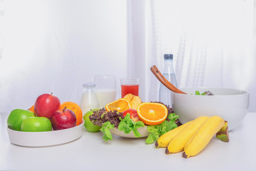 Fruits and vegetables, orange, banana, apple, milk and salad on the table white wood