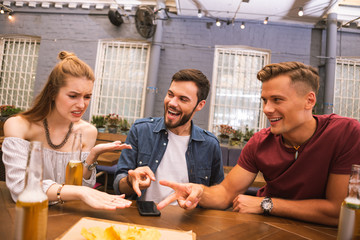 You lose. Cheerful young men looking at their friend while playing table games together