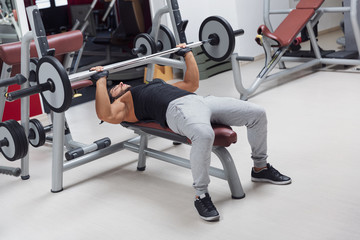 Plakat Weightlifter or bodybuilder lying on a bench lifting a barbell weight in a gym during training in a healthy active lifestyle and fitness concept