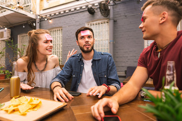 Explaining the word. Calm clever young man sitting between his best friends and thoughtfully looking into the distance while playing games with them