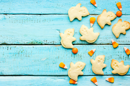 Halloween treats for kids - ghost cookies and sweet candy corn on a blue wooden background top view