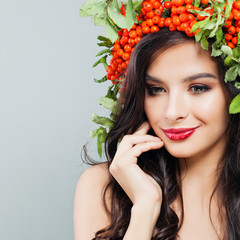 Cheerful brunette woman fashion model with healthy curly hairstyle, makeup and red berries and green leaves, portrait