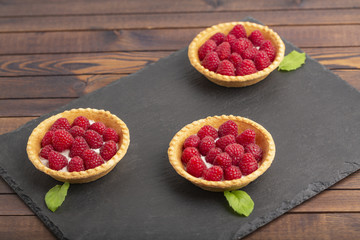 Tartlet with cream and fresh raspberries, served on a slate plate.
