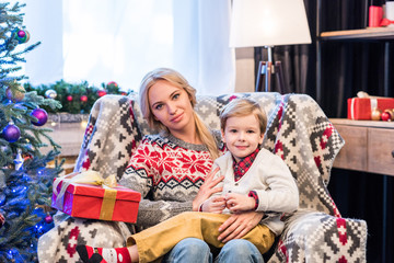 beautiful happy mother and son sitting together and smiling at camera at christmas time