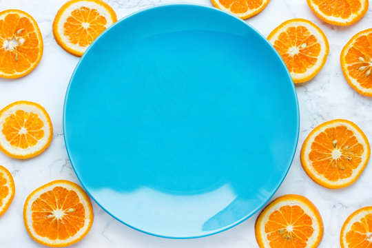 Empty blue plate over orange slices background top view, healthy food concept