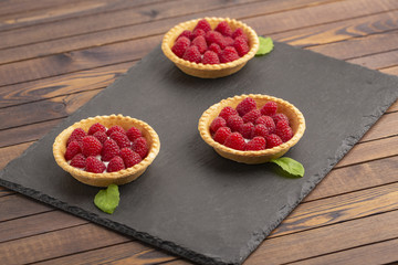 Tartlet with cream and fresh raspberries, served on a slate plate.