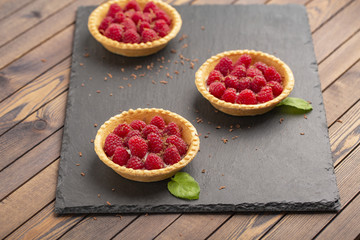 Tartlet with cream and fresh raspberries, served on a slate plate.